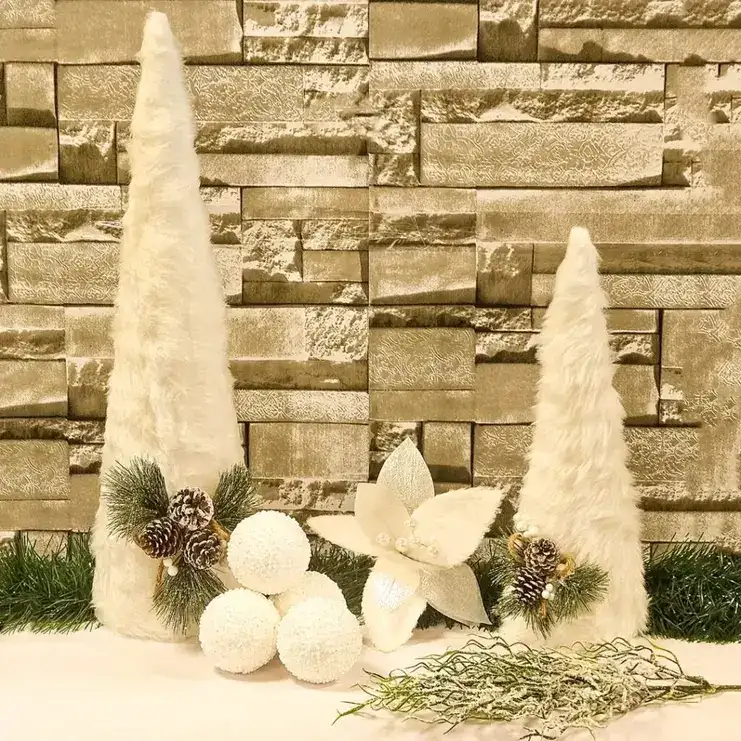 Duas árvores de Natal cônicas de pelúcia branca, com pinhas, flores e bolas de neve sobre fundo de pedra.