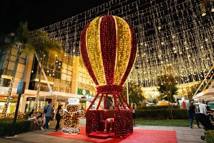 Balão de Natal gigante iluminado em vermelho e dourado, boneco de biscoito luminoso e teto de luzes em shopping.