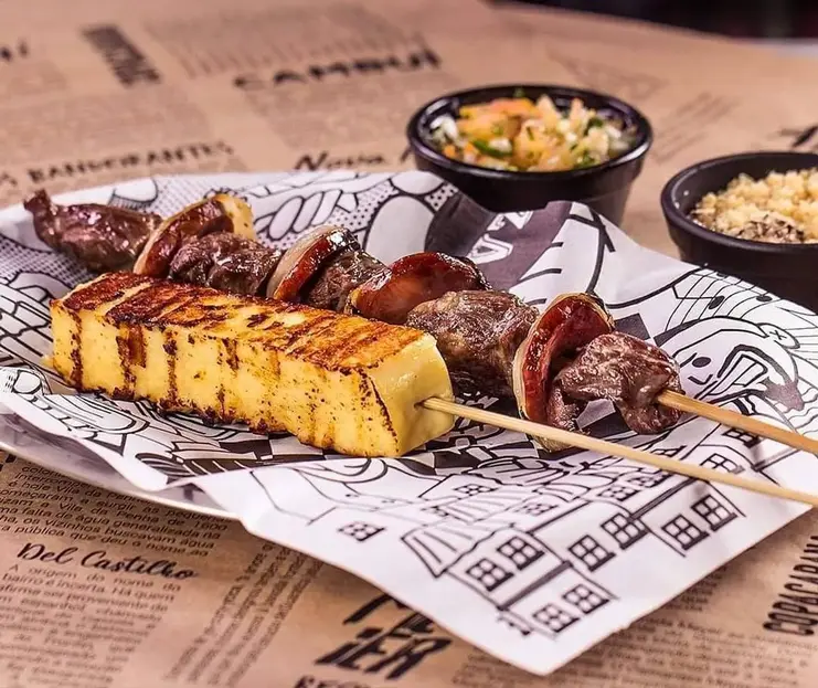 Snapinsta.app 116872065 648789552661446 4573271342556823458 n 1080 Espetinho de queijo coalho e espeto de carne com cebola grelhados na brasa, acompanhados de farofa e molho vinagrete.