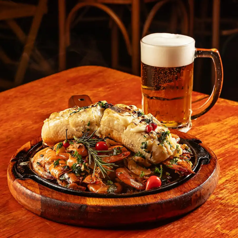 Prato gourmet com camarões grelhados, pão de alho e cerveja