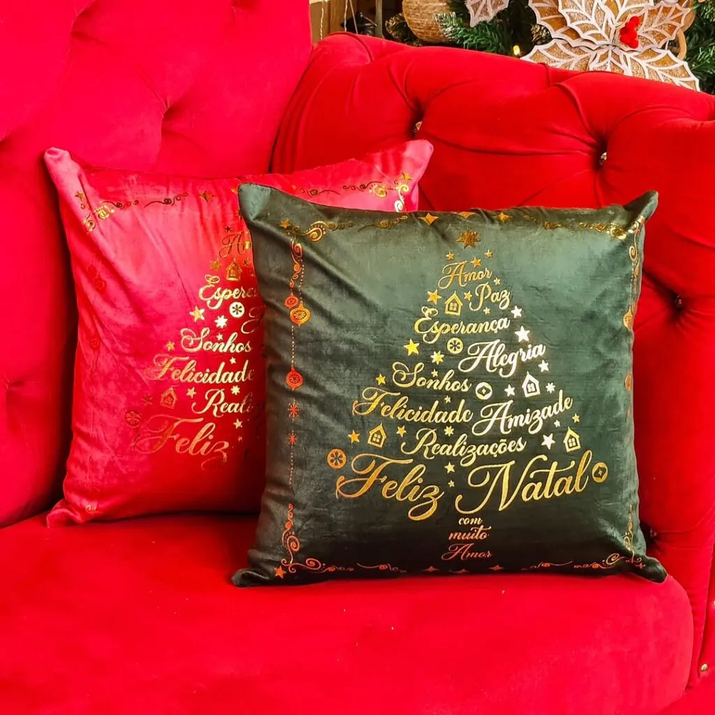 Almofadas de veludo verde e vermelha em sofá rubro, com estampas douradas de árvore de Natal formadas por palavras.