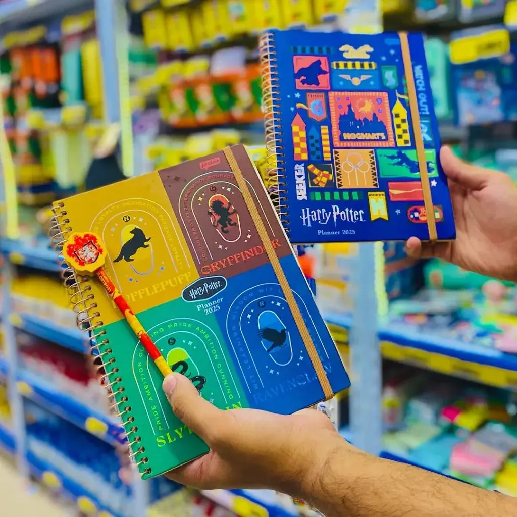 Dois planners Harry Potter 2025: um com os brasões das Casas de Hogwarts e outro azul com ilustrações temáticas de quadribol e o castelo.
