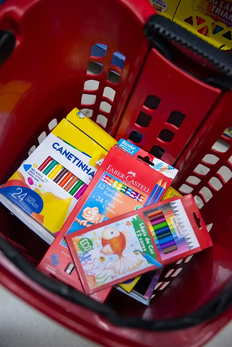 Cesto de compras vermelho com caixas de canetinhas e lápis de cor da Faber-Castell em seu interior.