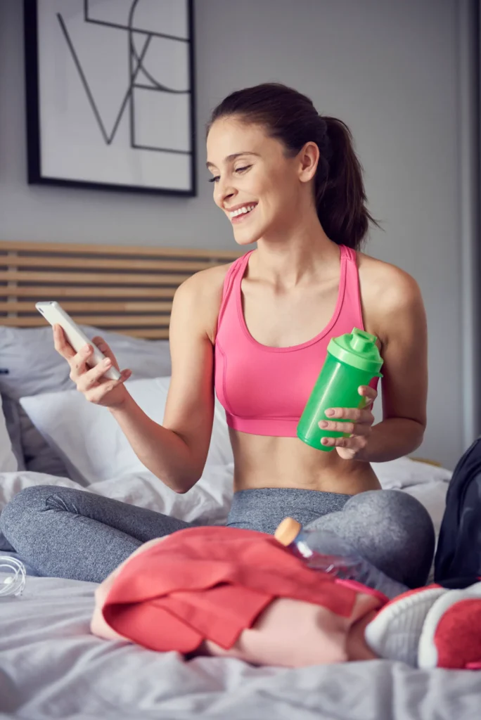 cheerful athlete using mobile phone bedroom Mulher sorridente com shaker e celular na cama