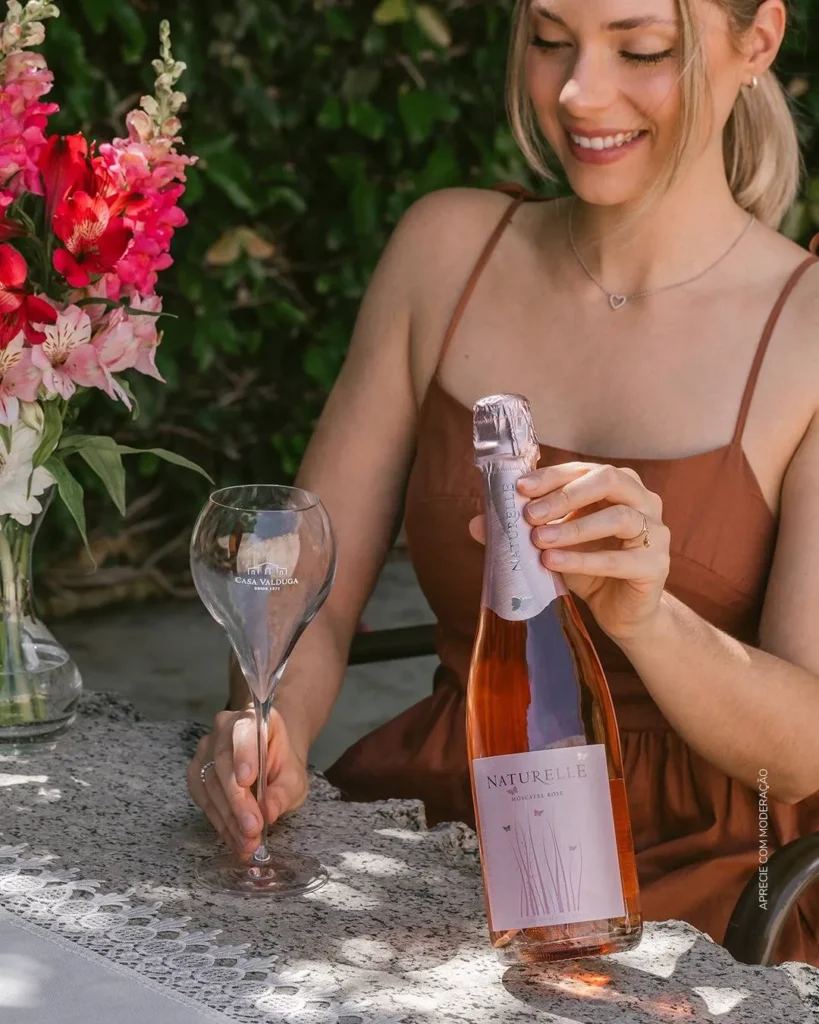 SaveClip.App 489996628 1077077241114892 6874713904529124752 n Mulher sorrindo com vinho rosé e flores ao fundo