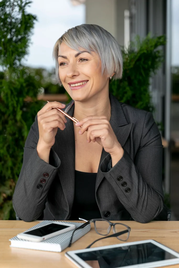 smiley woman table holding glasses Mulher sorrindo com caneta em mãos em escritório moderno
