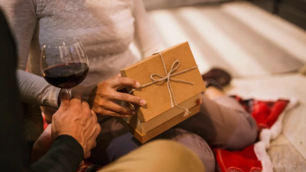 couple opening gifts together with glass wine Pessoa segurando presente e taça de vinho