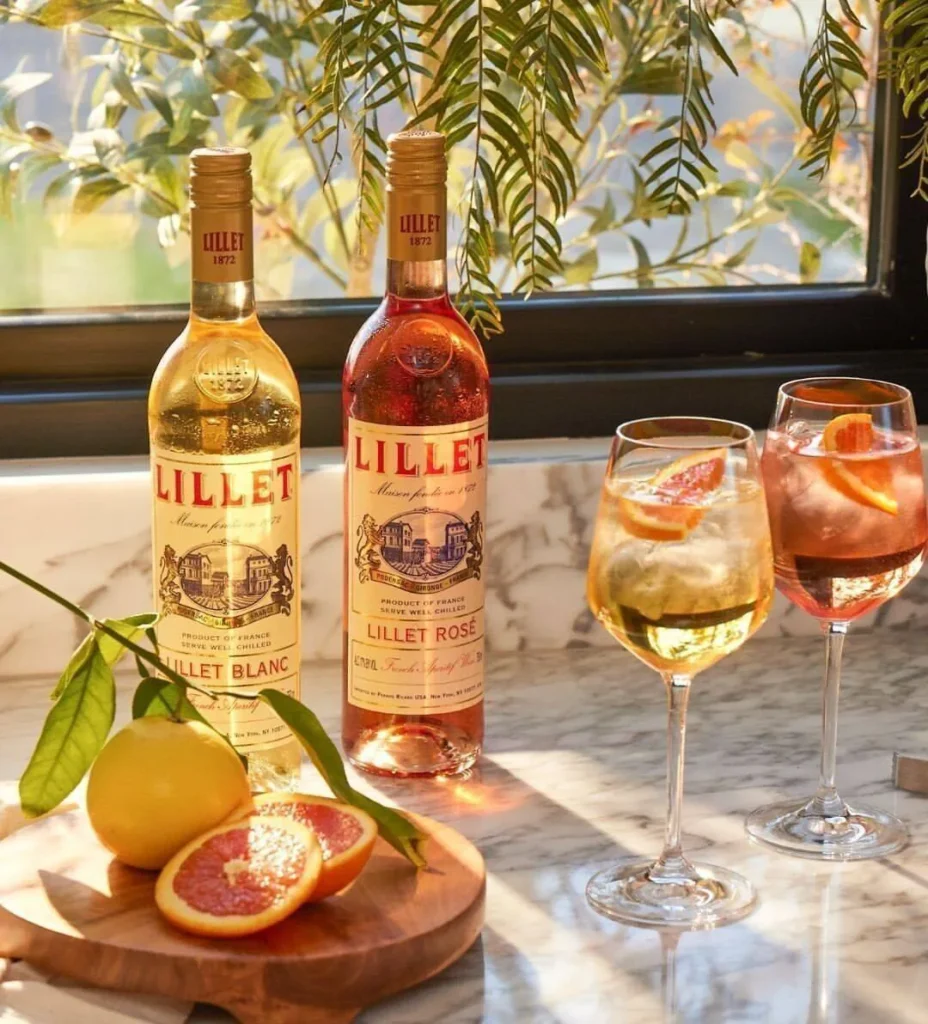 SaveClip.App 461314711 556616227040094 1681573808287402267 n Duas garrafas de Lillet e drinks com frutas em uma mesa