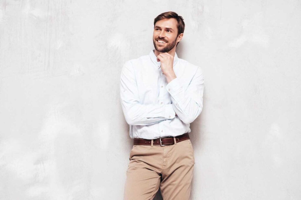 Homem sorridente de camisa clara contra parede neutra.