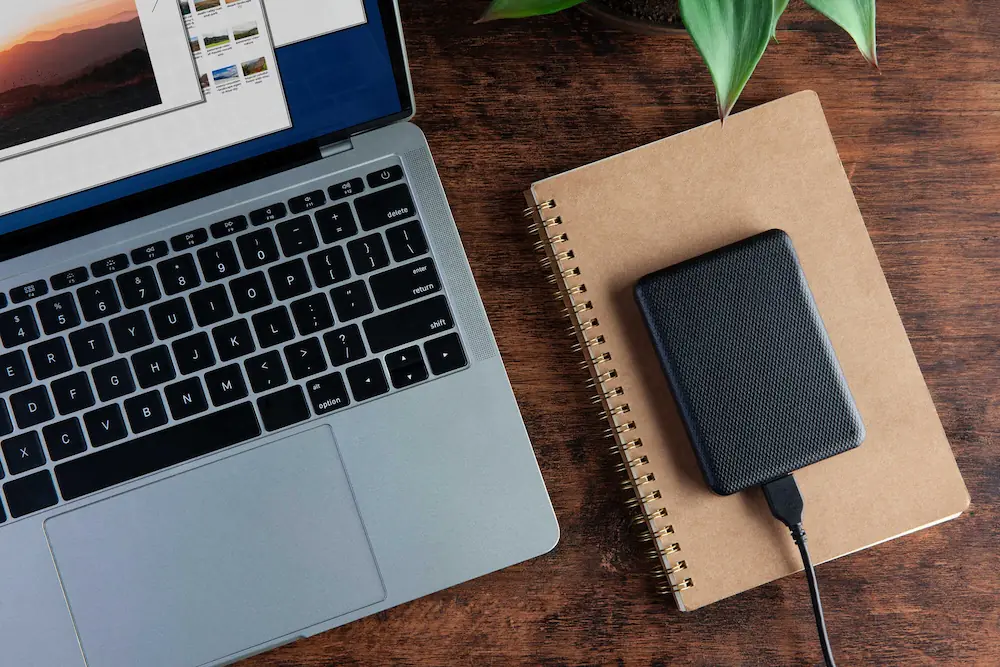 Laptop com disco rígido externo e caderno sobre mesa