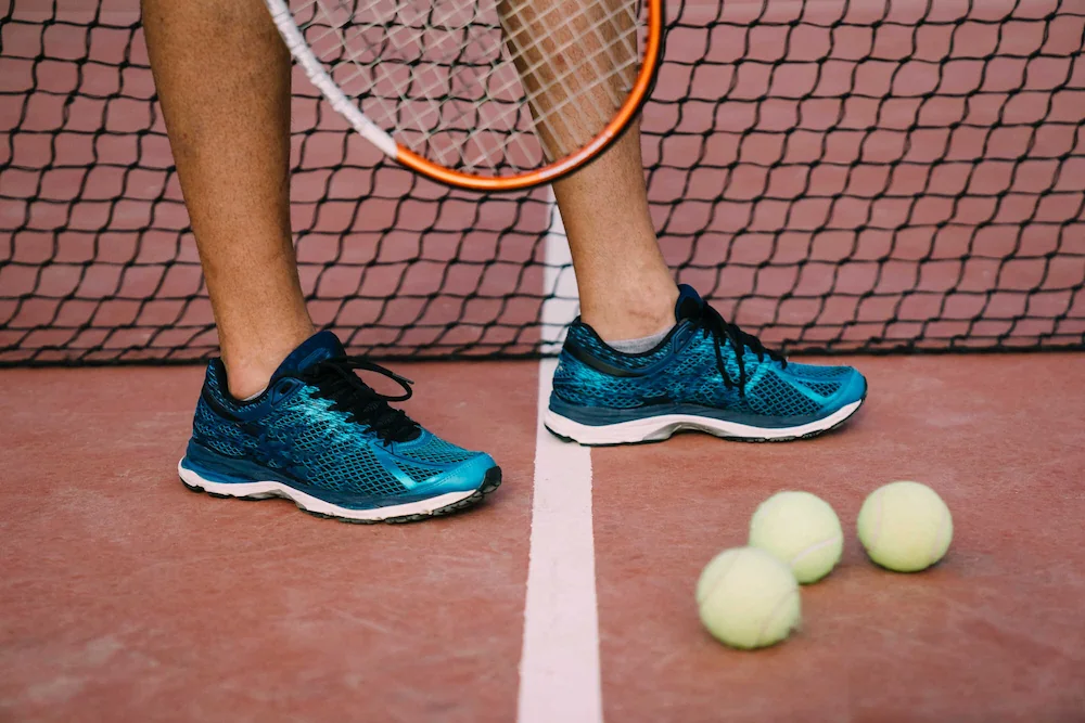 Tênis de corrida azul ao lado de tênis de tenis e bolas