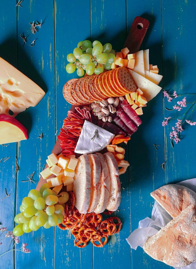 israel pina oZ Txnb8kQA unsplash Tábua de frios com queijos, frutas e pães variados.