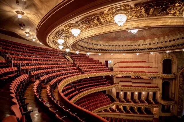 Interior de um teatro com assentos vermelhos e detalhes ornamentais.