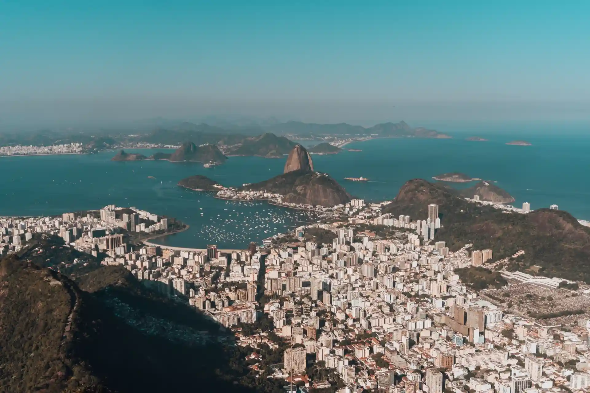Vista aérea do Pão de Açúcar e Baía de Guanabara com barcos e prédios no Rio de Janeiro em dia ensolarado.