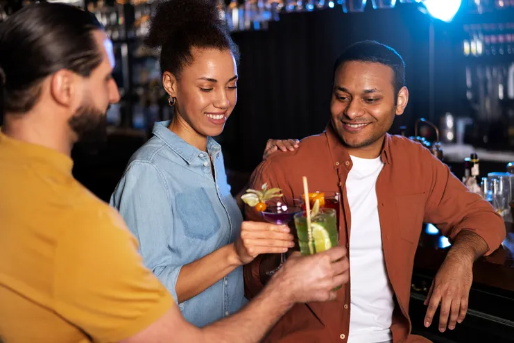 Grupo de amigos celebrando com drinks artesanais em um bar moderno. Close-up de pessoas brindando com coquetéis coloridos e sorrindo.