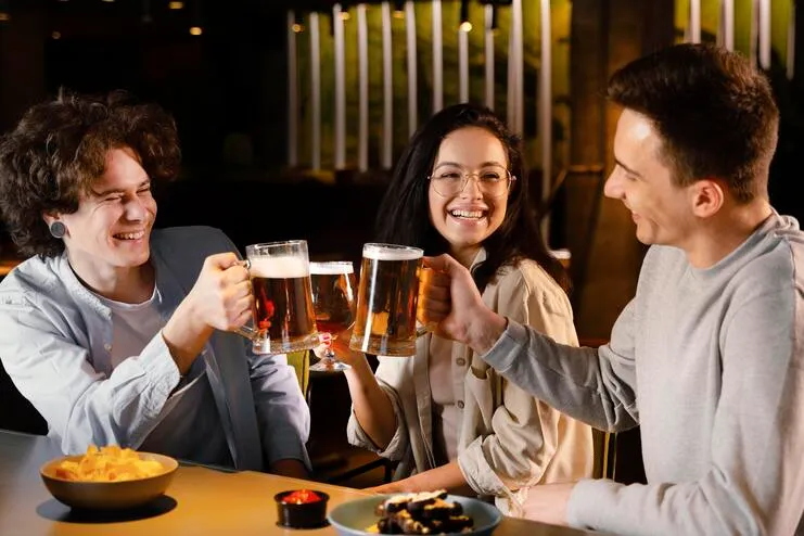 Grupo de amigos em um happy hour brindando com canecas de cerveja em um bar. Jovens sorrindo e celebrando com petiscos e bebidas em um ambiente acolhedor.