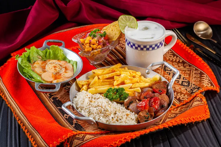 Lomo saltado com arroz e fritas, acompanhado de ceviche, batatas à huancaína e bebida sobre toalha andina.