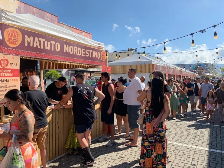 Fila de pessoas diante da barraca de madeira Matuto Nordestino em evento ao ar livre com luzes penduradas.