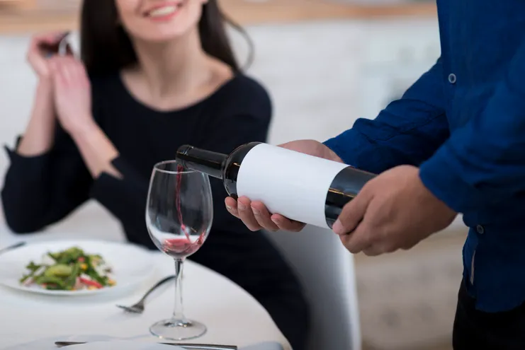 Garçom servindo vinho tinto a uma mulher em um restaurante.