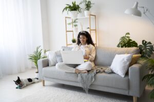 Mulher trabalhando em casa com laptop e cachorro próximo.