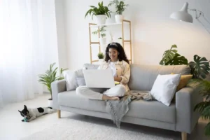Mulher trabalhando em casa com laptop e cachorro próximo.