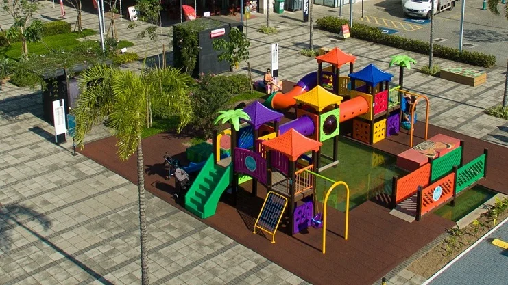 Vista aérea de playground colorido com escorregador e balanço instalados sobre piso emborrachado em praça urbana.