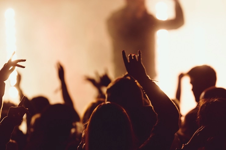 Silhueta de público com mãos para o alto fazendo sinal de rock em um show de música ao vivo com iluminação quente.