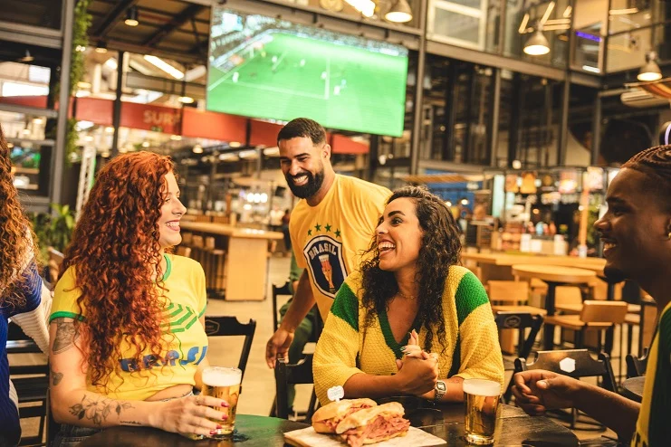 Amigos assistindo jogo em bar, comendo e bebendo