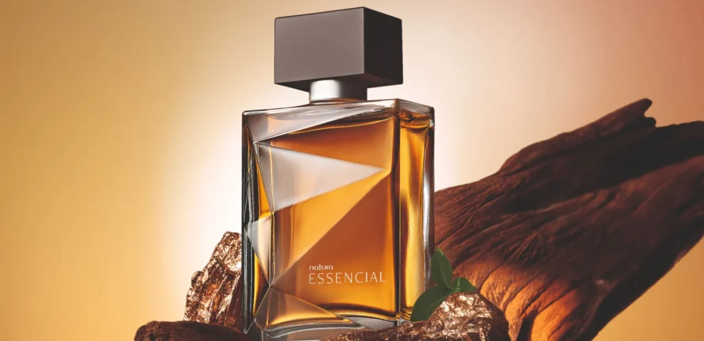 Frasco do perfume Natura Essencial masculino sobre pedaços de madeira rústica com fundo dourado iluminado.