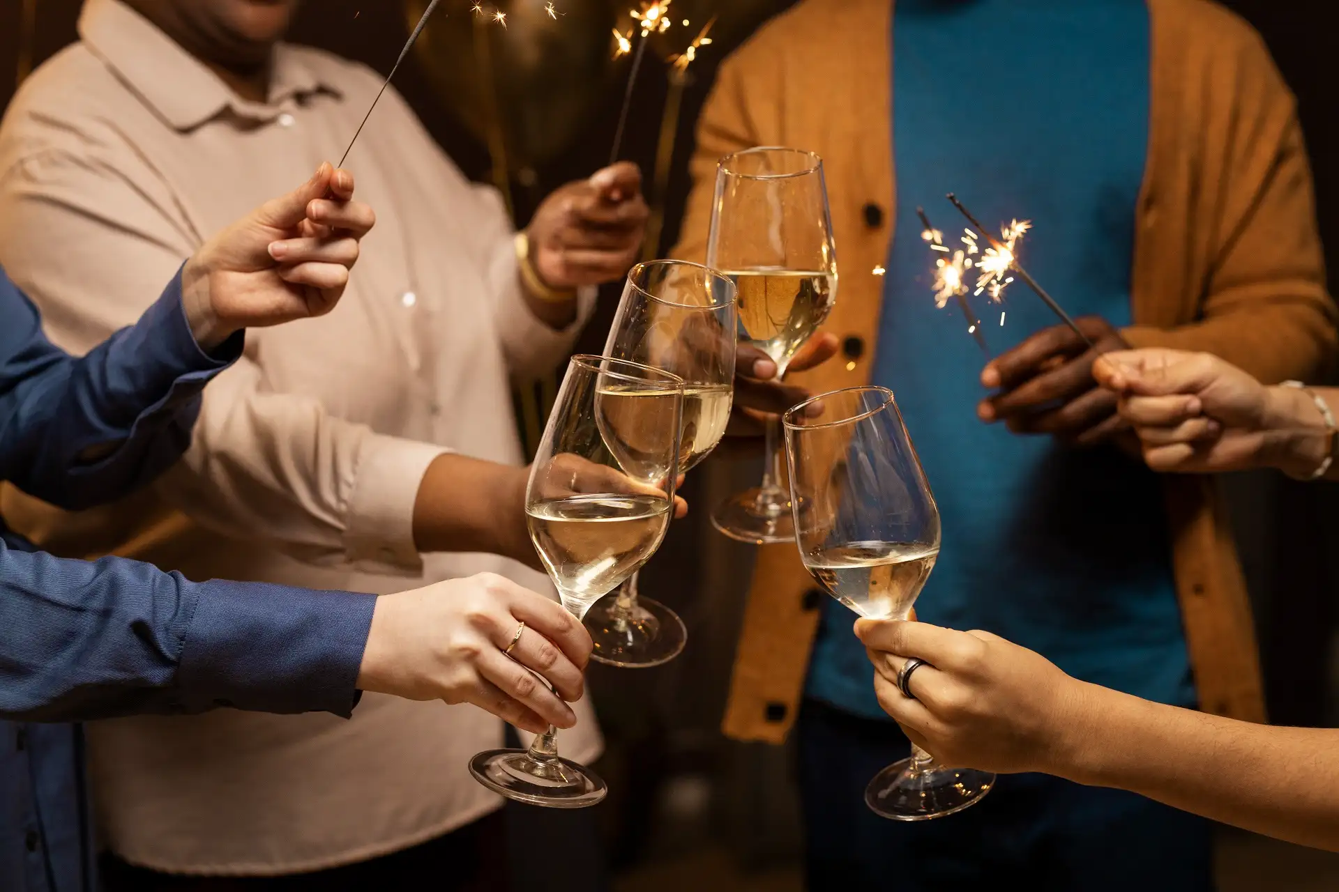Pessoas brindando com taças de espumante e acendendo velas faíscas em festa de celebração.