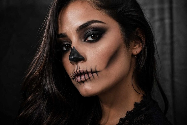 Mulher de cabelos escuros com maquiagem de caveira simples, nariz preto pintado e boca costurada.