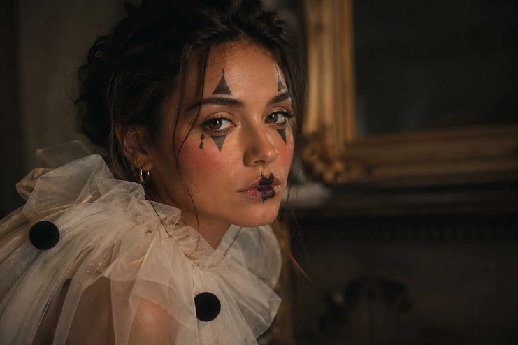 Mulher com gola bufante branca e maquiagem de pierrot com losangos pretos desenhados nos olhos.