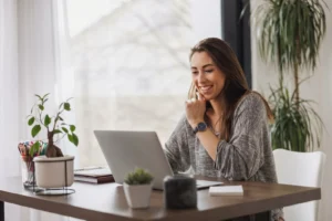 Mulher sorrindo e trabalhando em casa no computador.