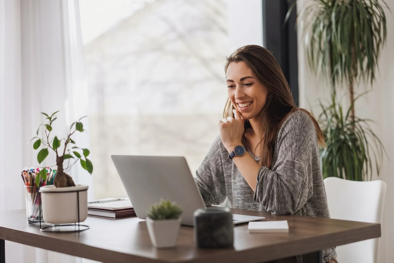 Mulher sorrindo e trabalhando em casa no computador.
