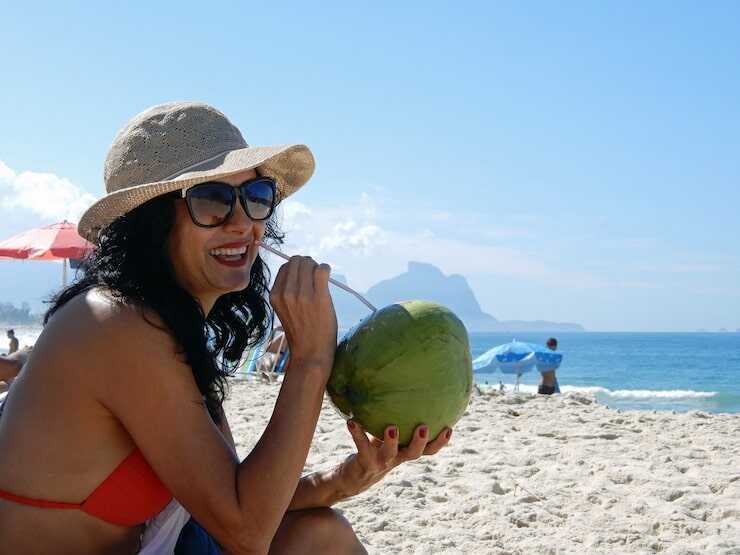 Mulher bebendo água de coco na praia.