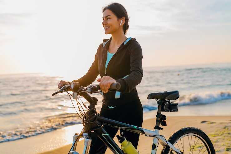 Mulher feliz pedalando bicicleta na praia ao pôr do sol.
