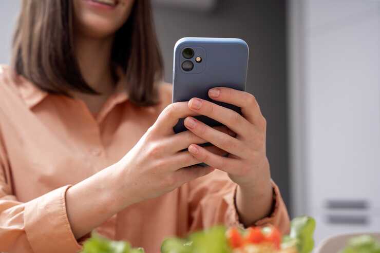 Mulher segurando smartphone em ambiente de refeição.