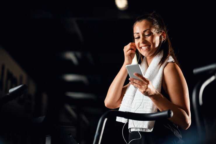 Mulher sorrindo enquanto usa o celular na academia.