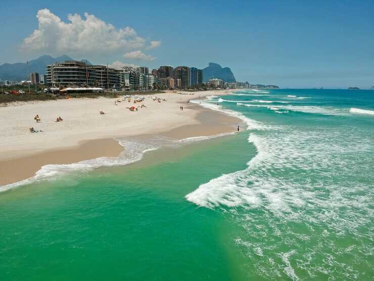 Praia com água verde e edifícios ao fundo.