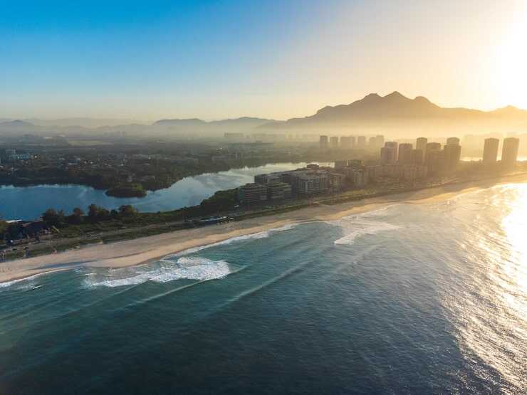 Vista aérea de praia ao amanhecer com montanhas ao fundo.