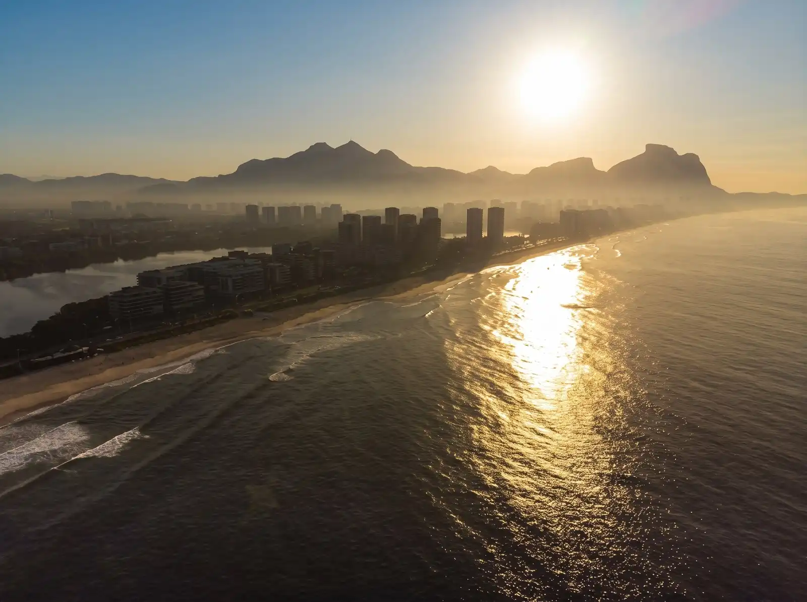 Vista aérea da praia ao pôr do sol em direção às montanhas.