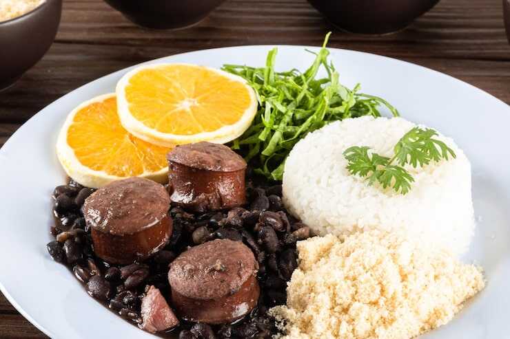 Prato de feijoada com arroz, linguiça e laranja.